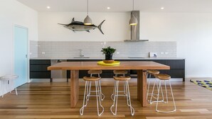 A modern kitchen with a wooden island, bar stools, pendant lighting, and a shark-themed wall decoration. - On The Beach (Lorne)