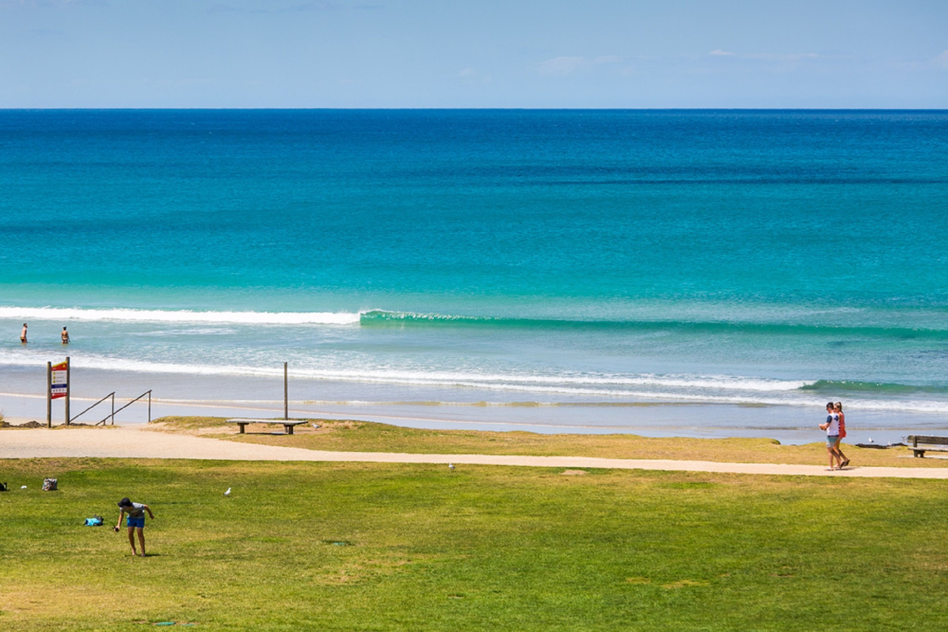 Una playa con césped, un banco y un cartel.