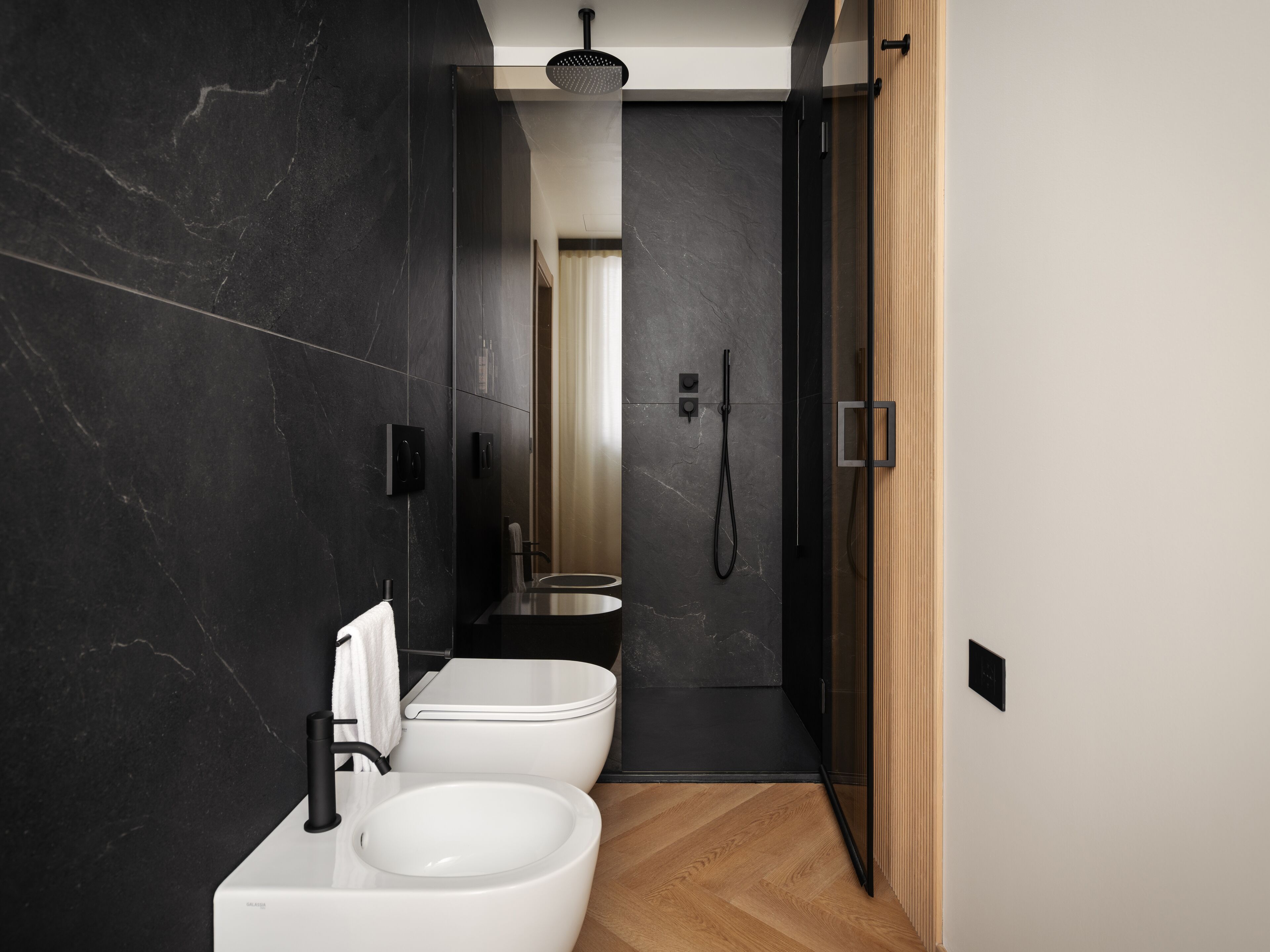 A modern bathroom with a black marble wall, a white sink, and a shower area.