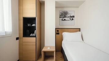 A compact hotel room with a bed, a small bedside table, a wardrobe, and a wall-mounted artwork.