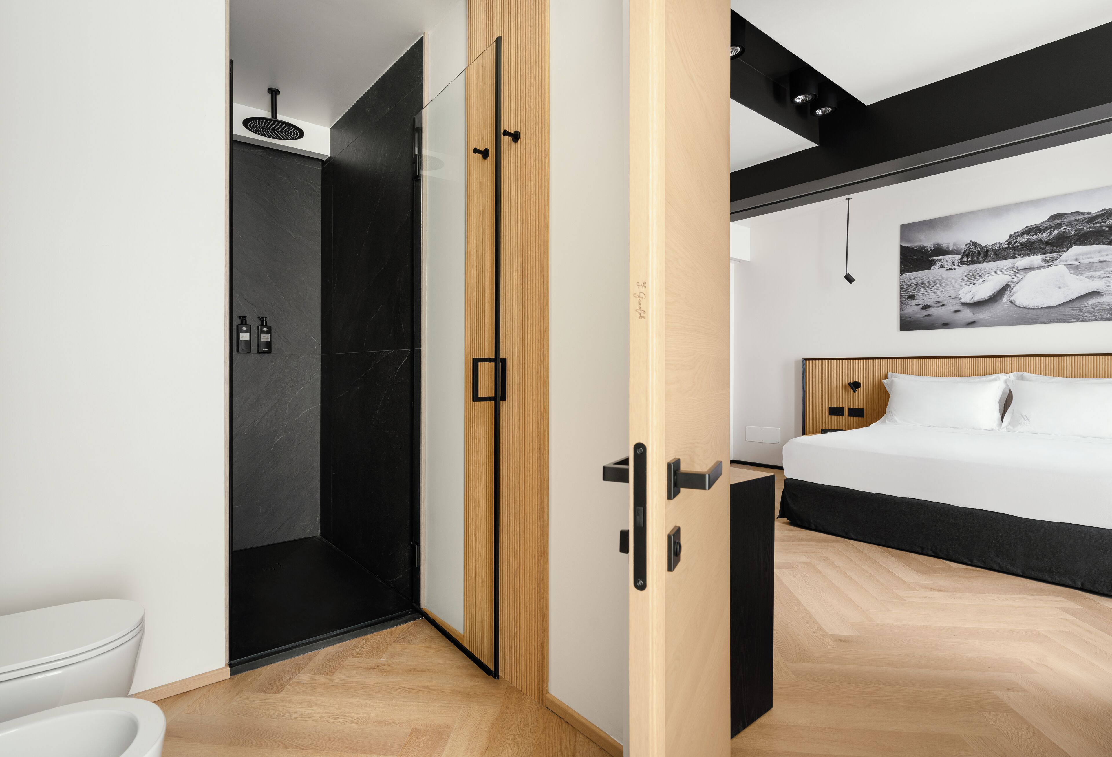 A modern bedroom with a large bed, a wooden door, and a shower area.