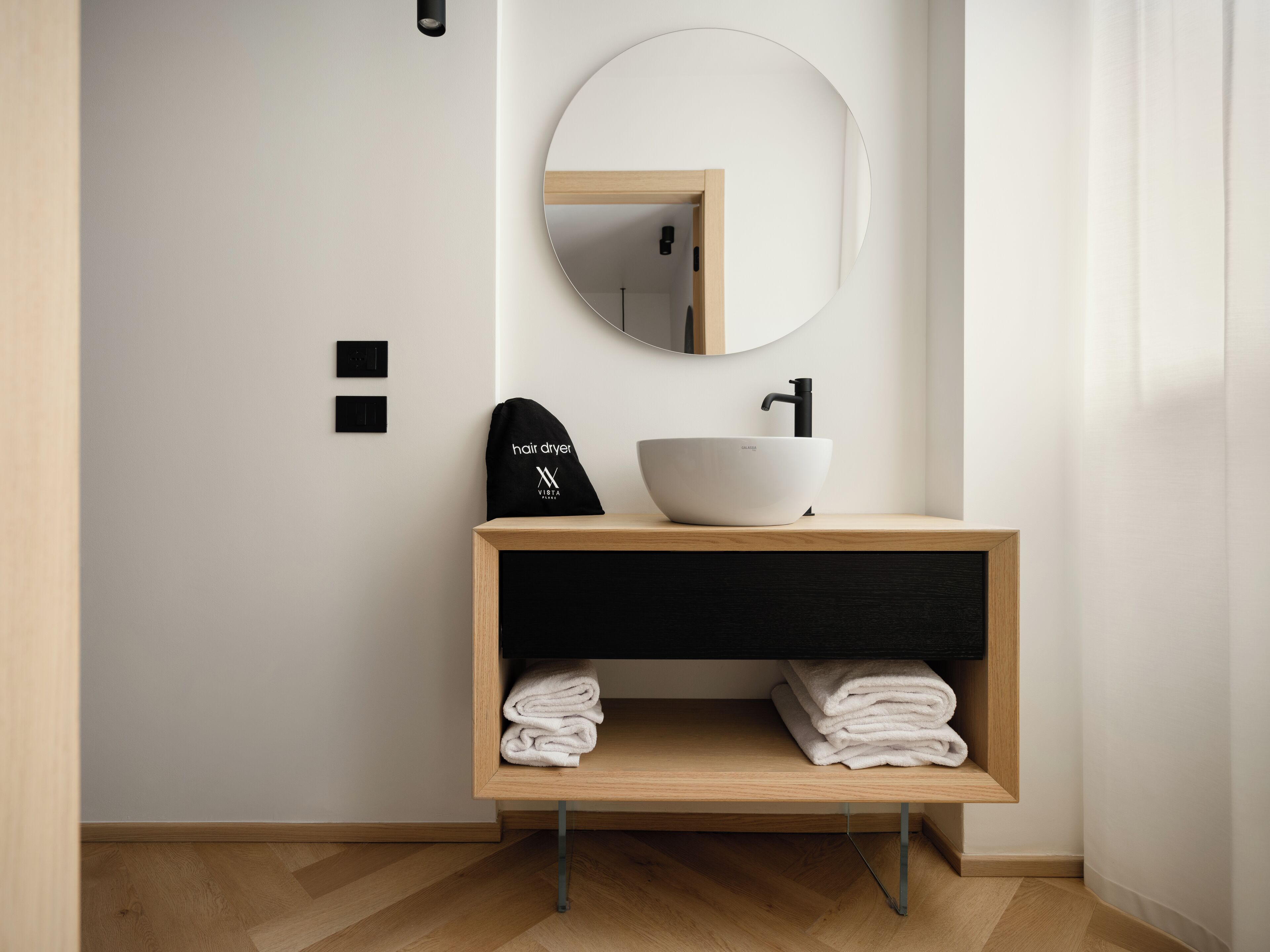 A modern bathroom with a white basin, a round mirror, and a towel rack.