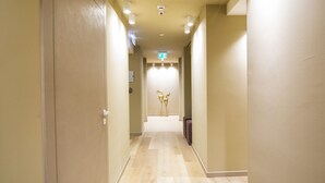 A hotel hallway with a light wood floor, beige walls, and a green exit sign. - View Place & Spa (Numana)