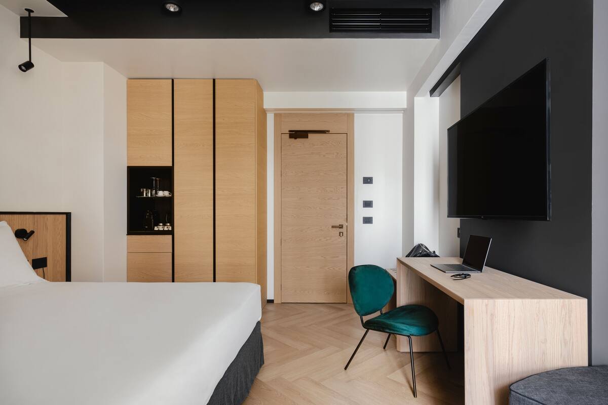 A modern hotel room with a bed, a desk with a laptop, a TV, and a wardrobe.