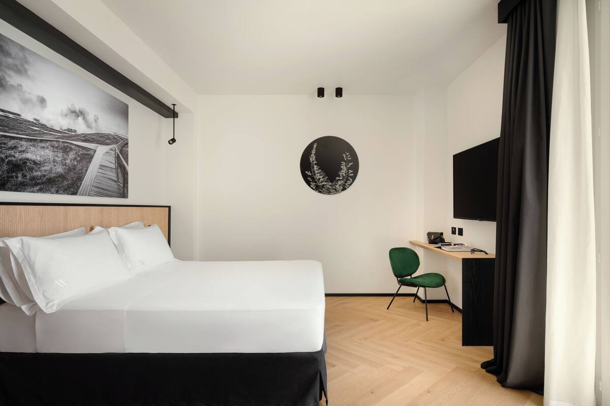 A modern hotel room with a large bed, a desk, a chair, and a wall-mounted TV.