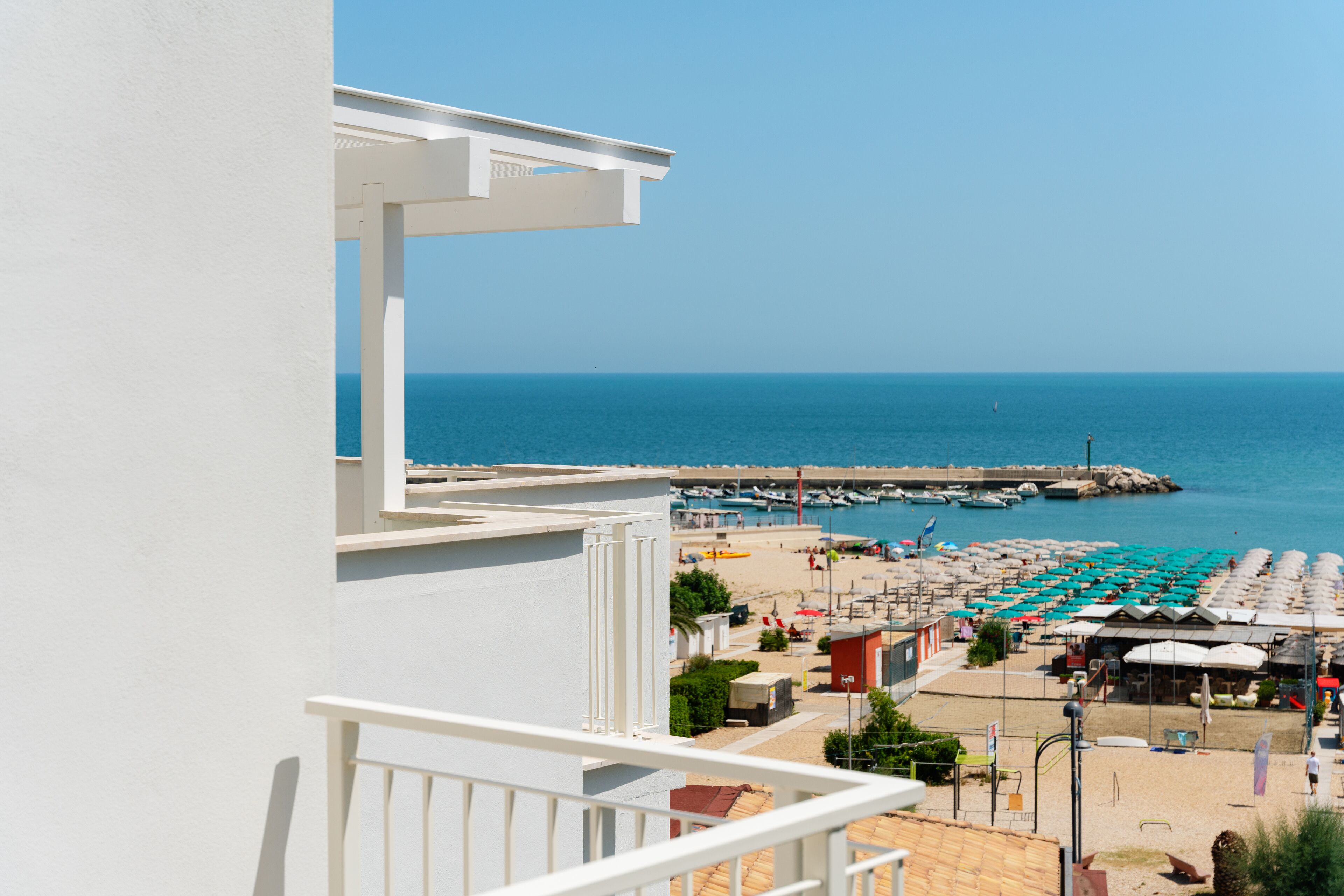 Uma varanda com vista para uma praia, um cais e barcos.