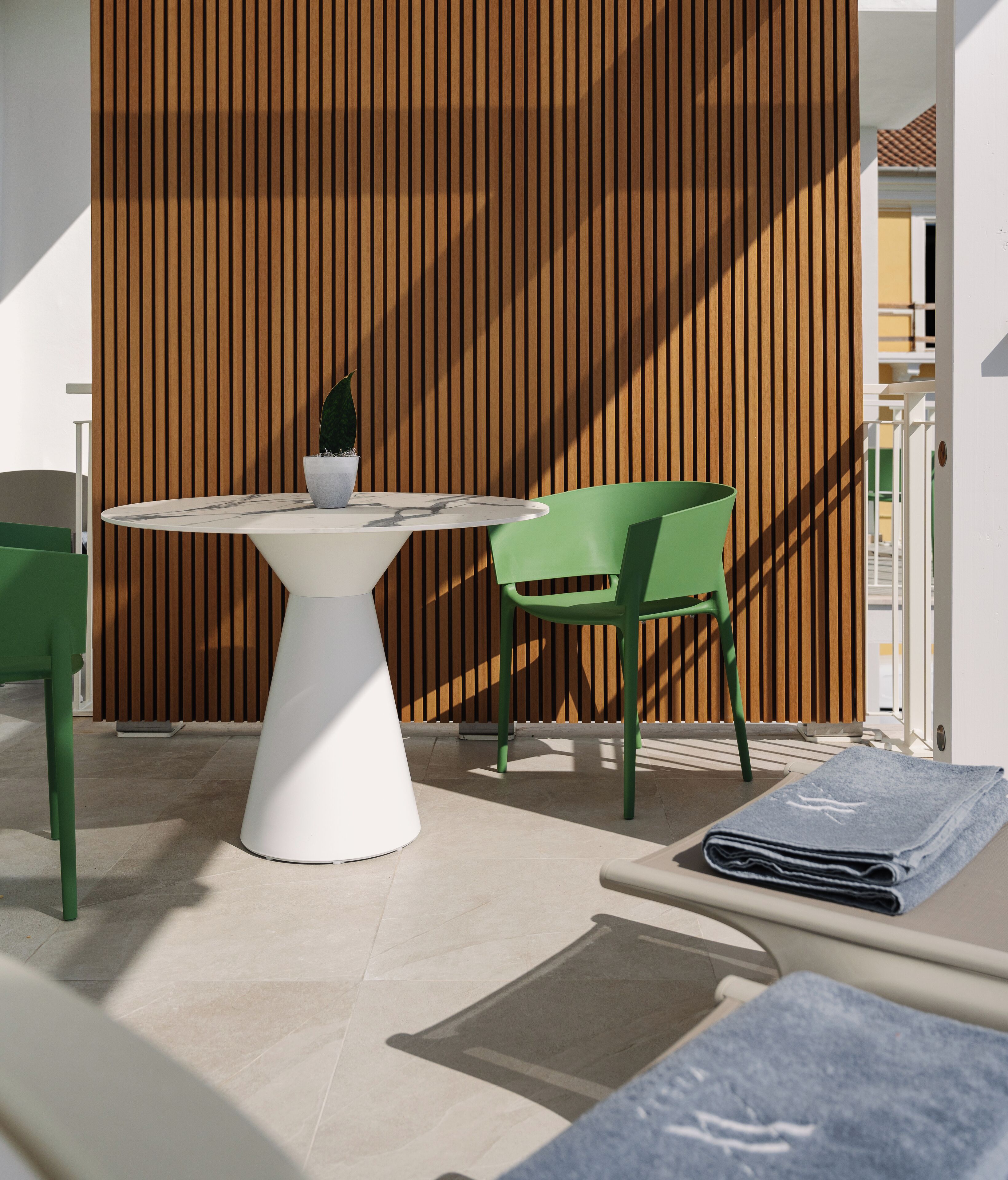 Un área de estar exterior moderna con una mesa blanca, una silla verde y una planta en maceta.