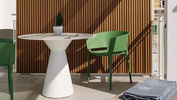 Un área de estar exterior moderna con una mesa blanca, una silla verde y una planta en maceta.