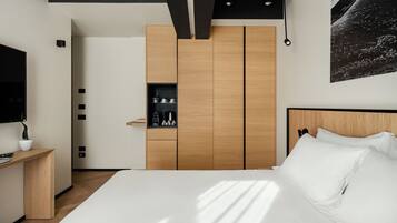 Un dormitorio moderno con una cama grande, un armario de madera, un estante pequeño con artículos de aseo y un televisor montado.