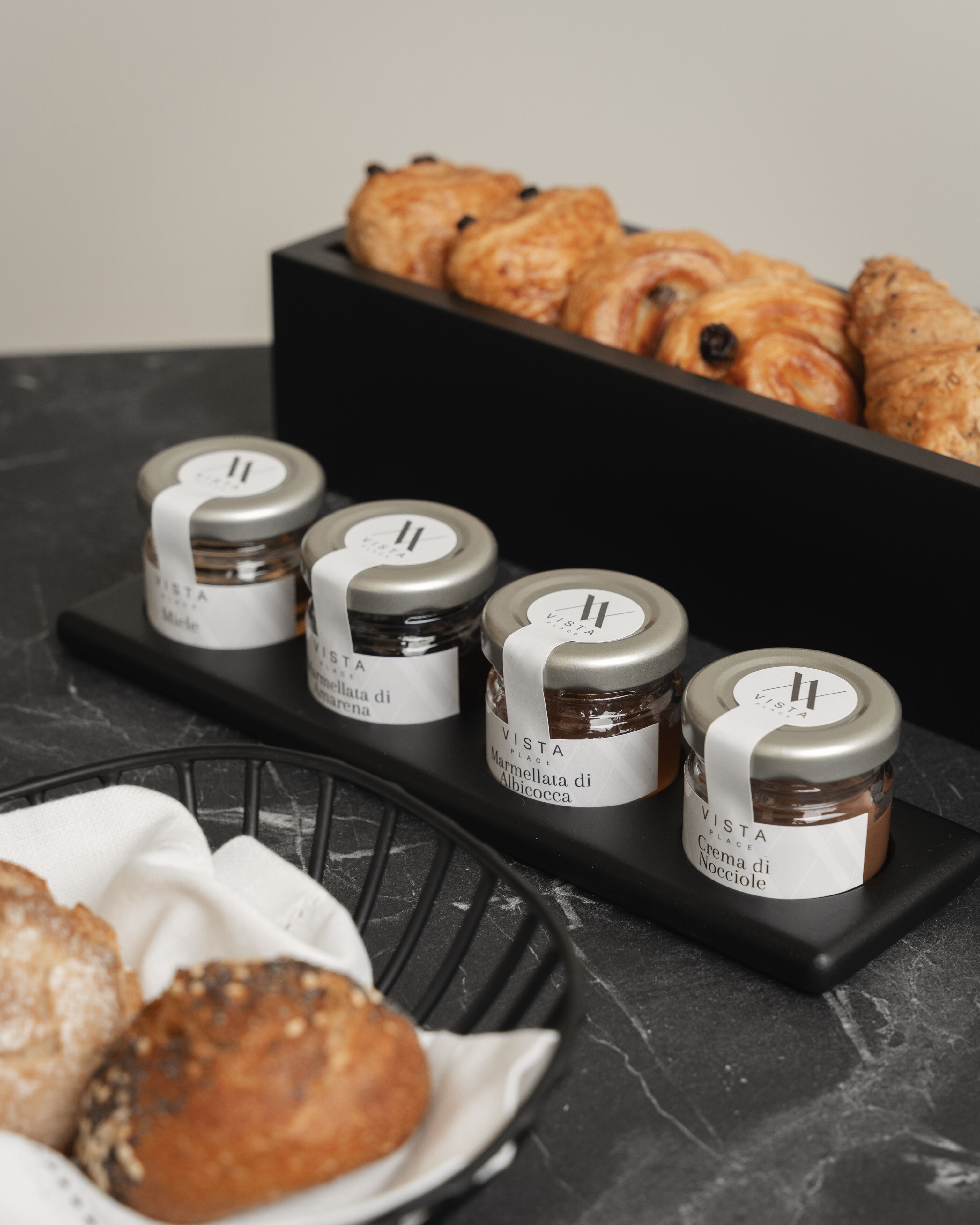 A display of food items including jars of marmellata di albicocca and nocioloe, along with pastries on a black tray.