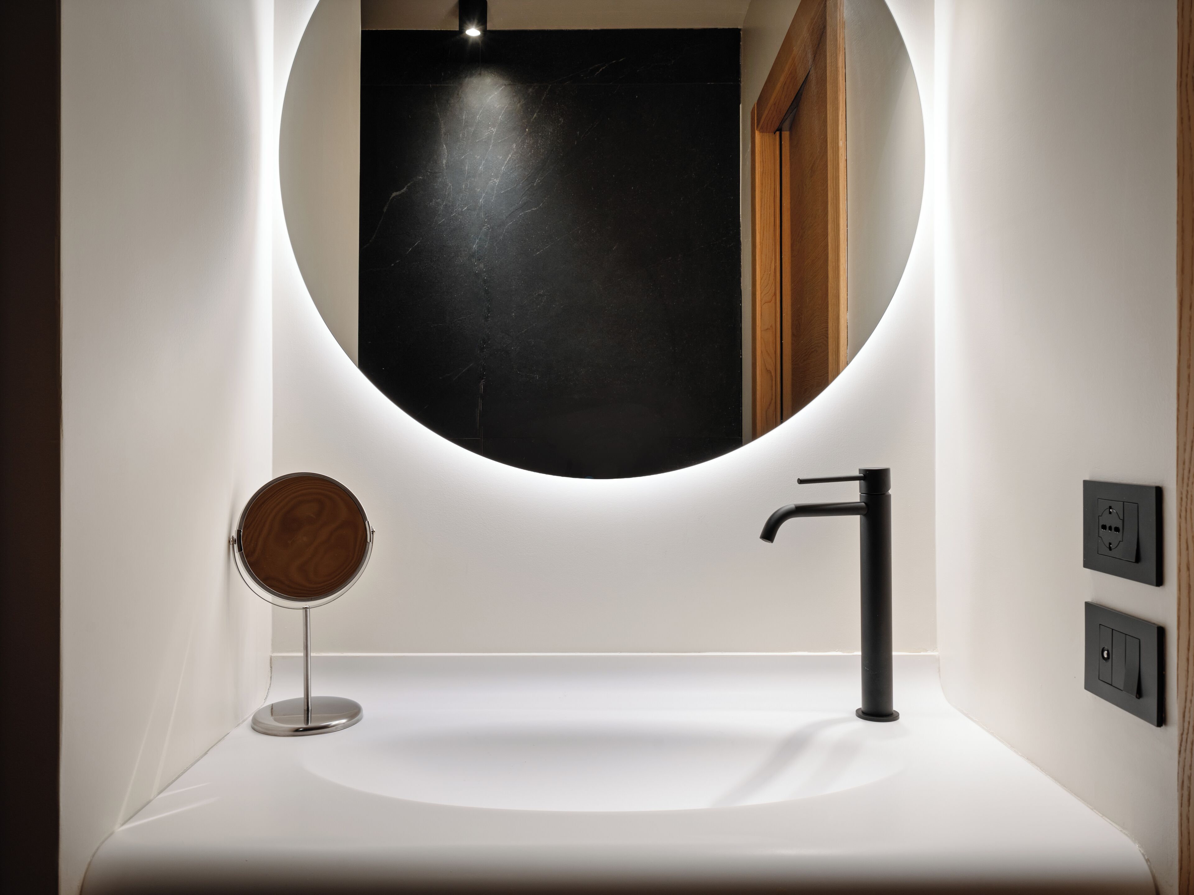 A modern bathroom with a white sink, a black faucet, and a round mirror.