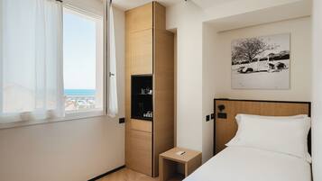 Une chambre d’hôtel comprenant un lit, une petite table de chevet, une armoire, une fenêtre avec des rideaux et une œuvre d’art accrochée au mur.