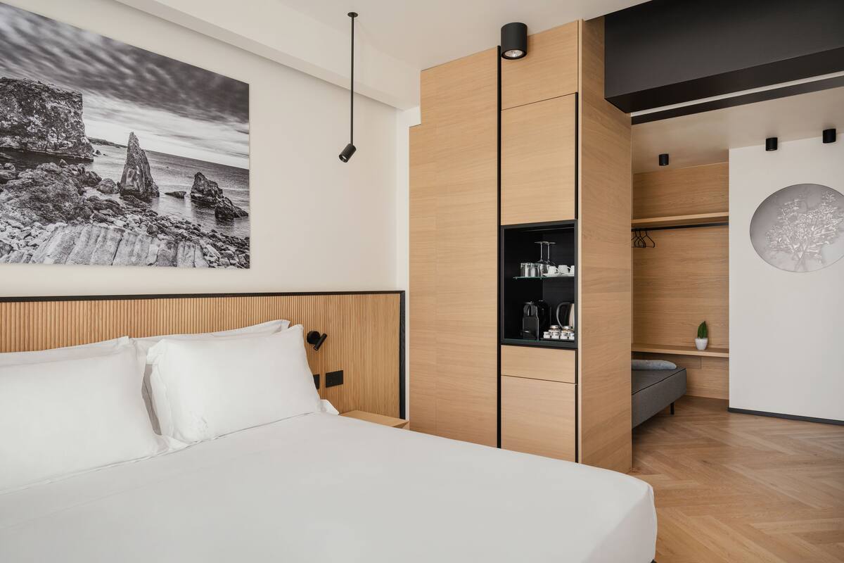 A modern bedroom with a bed, a wooden wardrobe, a built-in coffee machine, and a wall-mounted shelf.