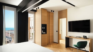 A modern hotel room with a large bed, a desk with a chair, a TV, and a view of the sea. - View Place & Spa (Numana)