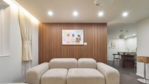 Una sala de estar moderna con un sofá, un muro decorativo de madera y una cocina al fondo.