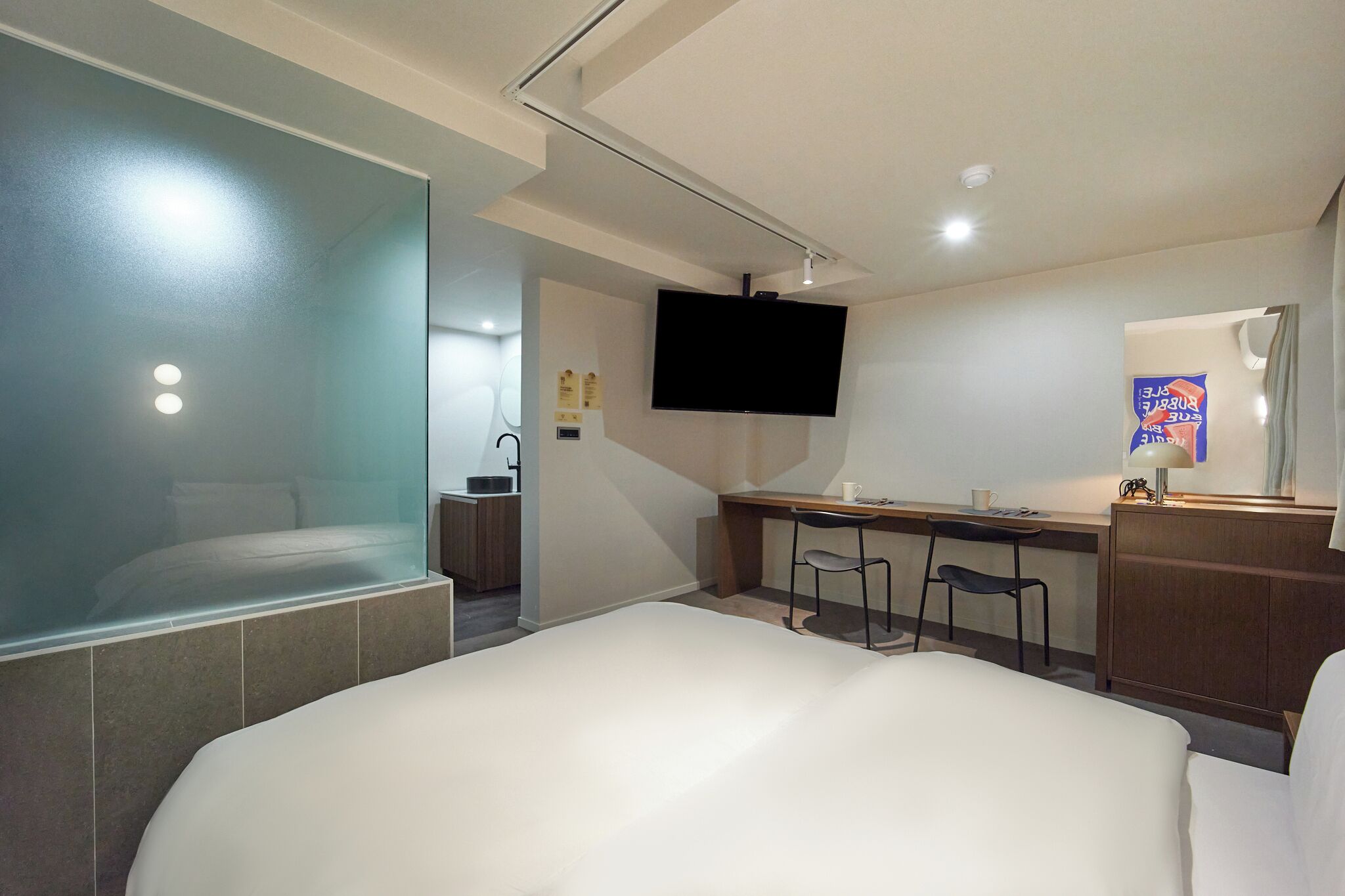 Habitación de hotel moderna con una cama grande, un escritorio con silla, televisor y una pequeña kitchenette.