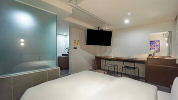 Habitación de hotel moderna con una cama grande, un escritorio con silla, televisor y una pequeña kitchenette.