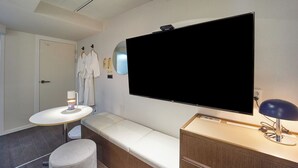 Un baño moderno con un espejo grande, un televisor de pantalla plana, un espejo redondo, un lavabo blanco y un banco.