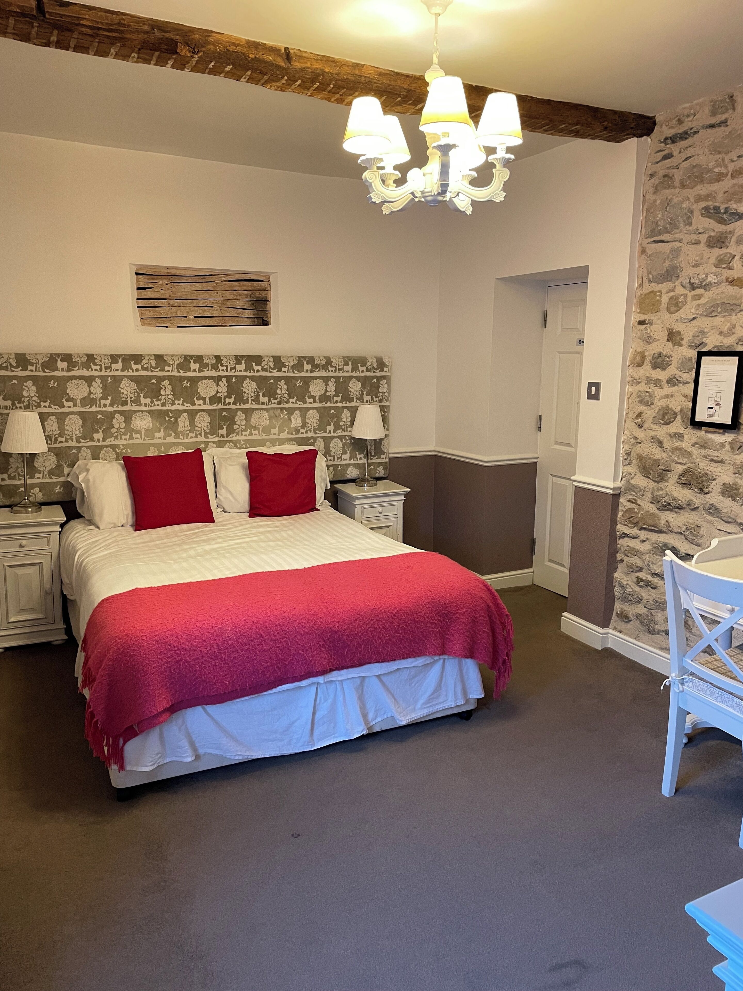 A bedroom with a bed, nightstands, a chandelier, a stone wall, and a door.