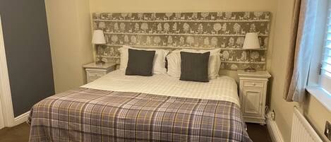 A neatly made bed with a plaid bedspread, two pillows, and a headboard with a nature-themed wallpaper. There are bedside lamps and a nightstand with a lamp.
