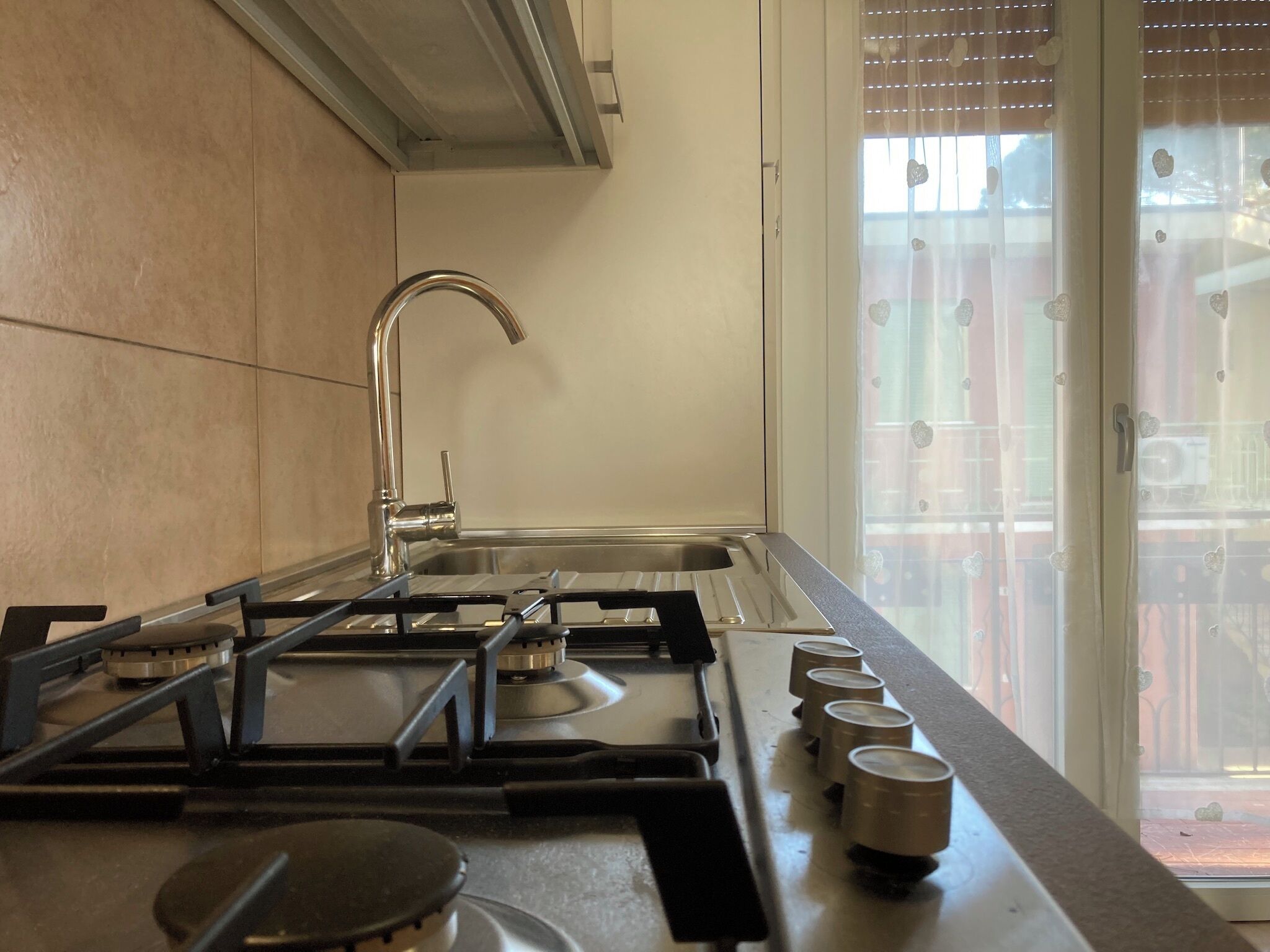A modern kitchen with a stainless steel sink, a gas stove, and a window with blinds.