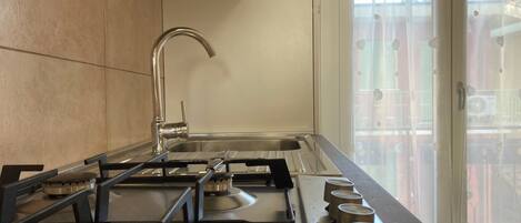 A modern kitchen with a stainless steel sink, a gas stove, and a window with blinds.