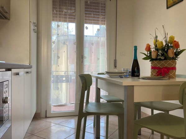 Ein Essbereich mit Tisch, Stühlen, einer Blumenvase und einer Flasche.