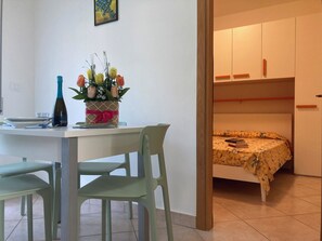 Ein kleiner, kompakter Wohnraum mit Küchenzeile, einem Essbereich mit Tisch und Stühlen sowie einem Bett mit gemustertem Überwurf.