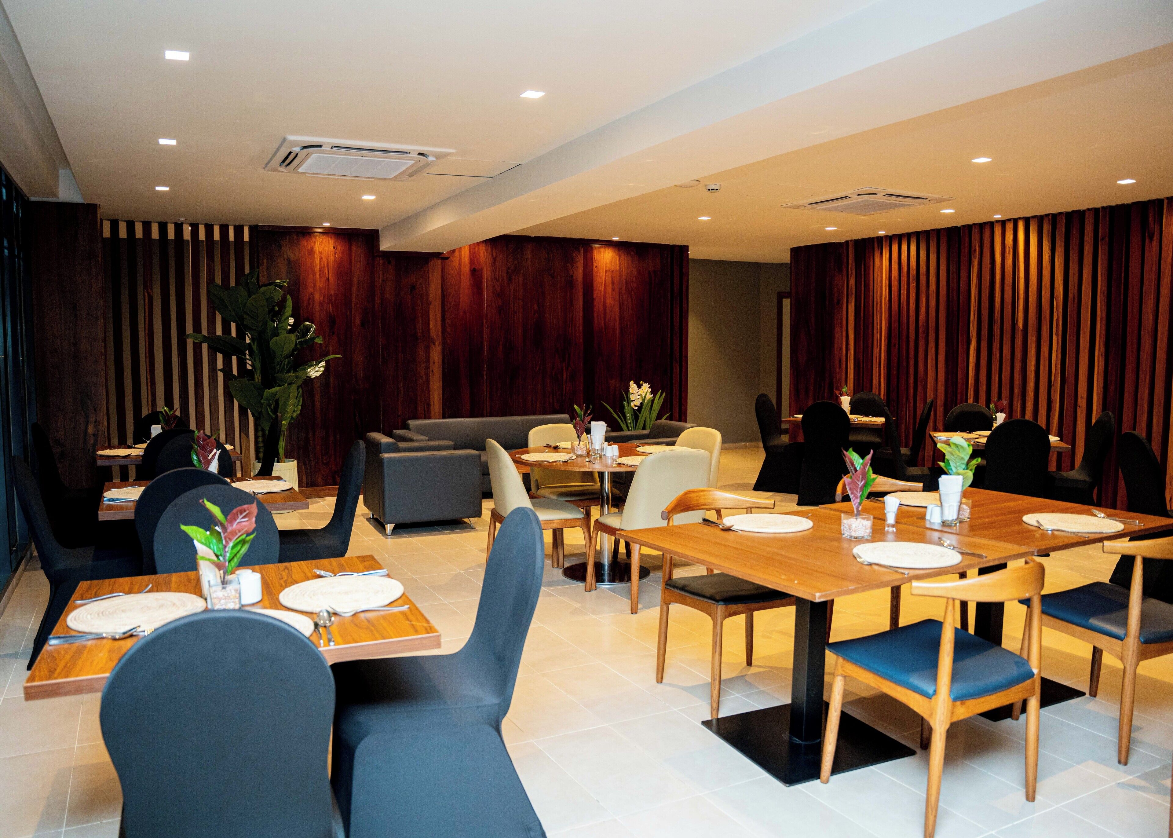 A modern dining area with wooden tables, blue chairs, and dark wood paneling on the walls.