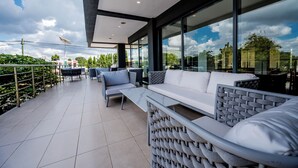 A modern outdoor patio with a white sofa, wicker chairs, and a glass railing overlooking a cityscape. - Urban by CityBlue Hotel, Dar es Salaam (Dar es Salaam)