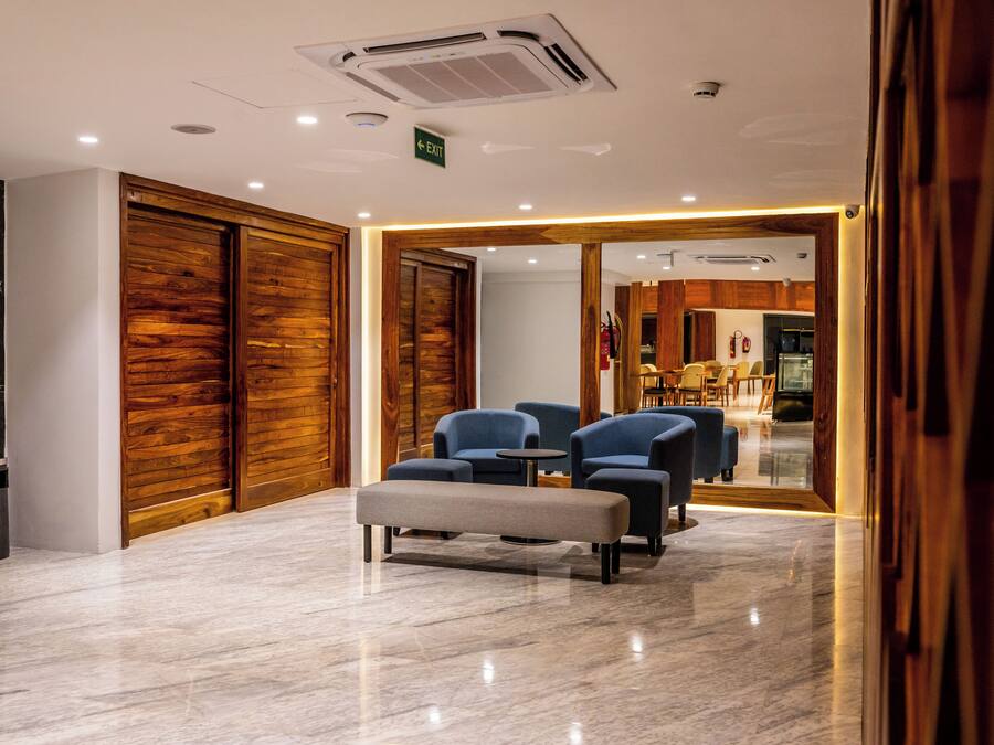 Un hall d’entrée avec un sol en marbre, des portes en bois et un espace détente aux sièges bleus.
