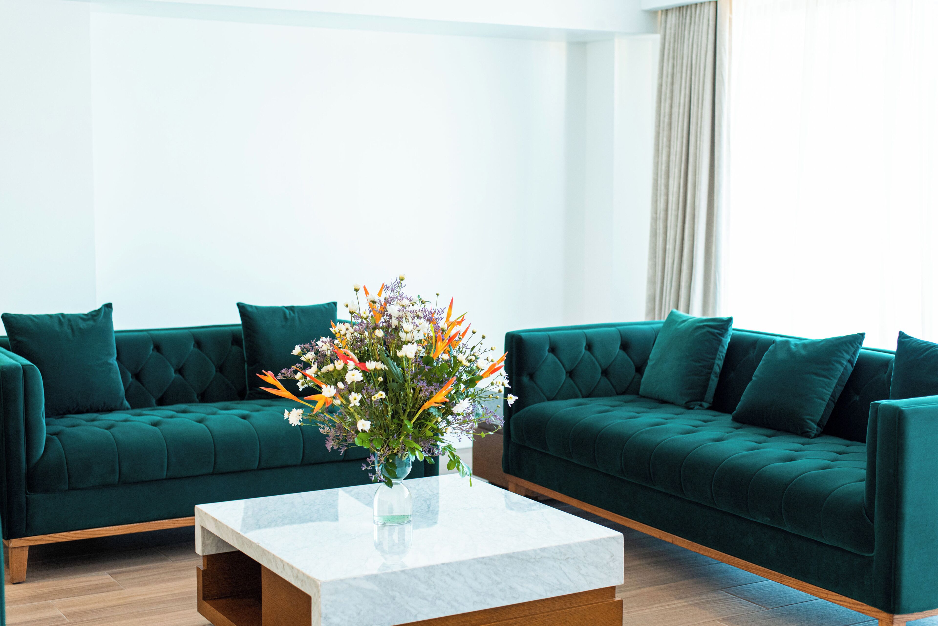 A modern living room with two green sofas, a marble coffee table, and a vase of flowers.