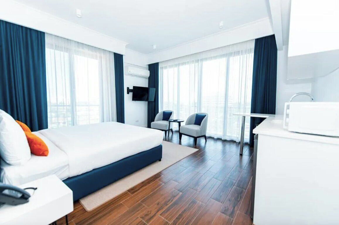 A modern hotel room with a large bed, a desk, two chairs, and a TV.