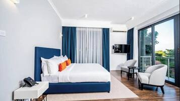 Una habitación de hotel moderna con una cama grande, un escritorio con teléfono, un televisor y un balcón con vistas.