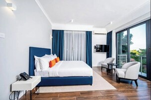 Una habitación de hotel moderna con una cama grande, un escritorio con teléfono, un televisor y un balcón con vistas.