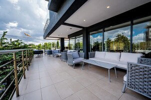 An outdoor patio with modern seating, large windows, and a view of the surrounding greenery.
