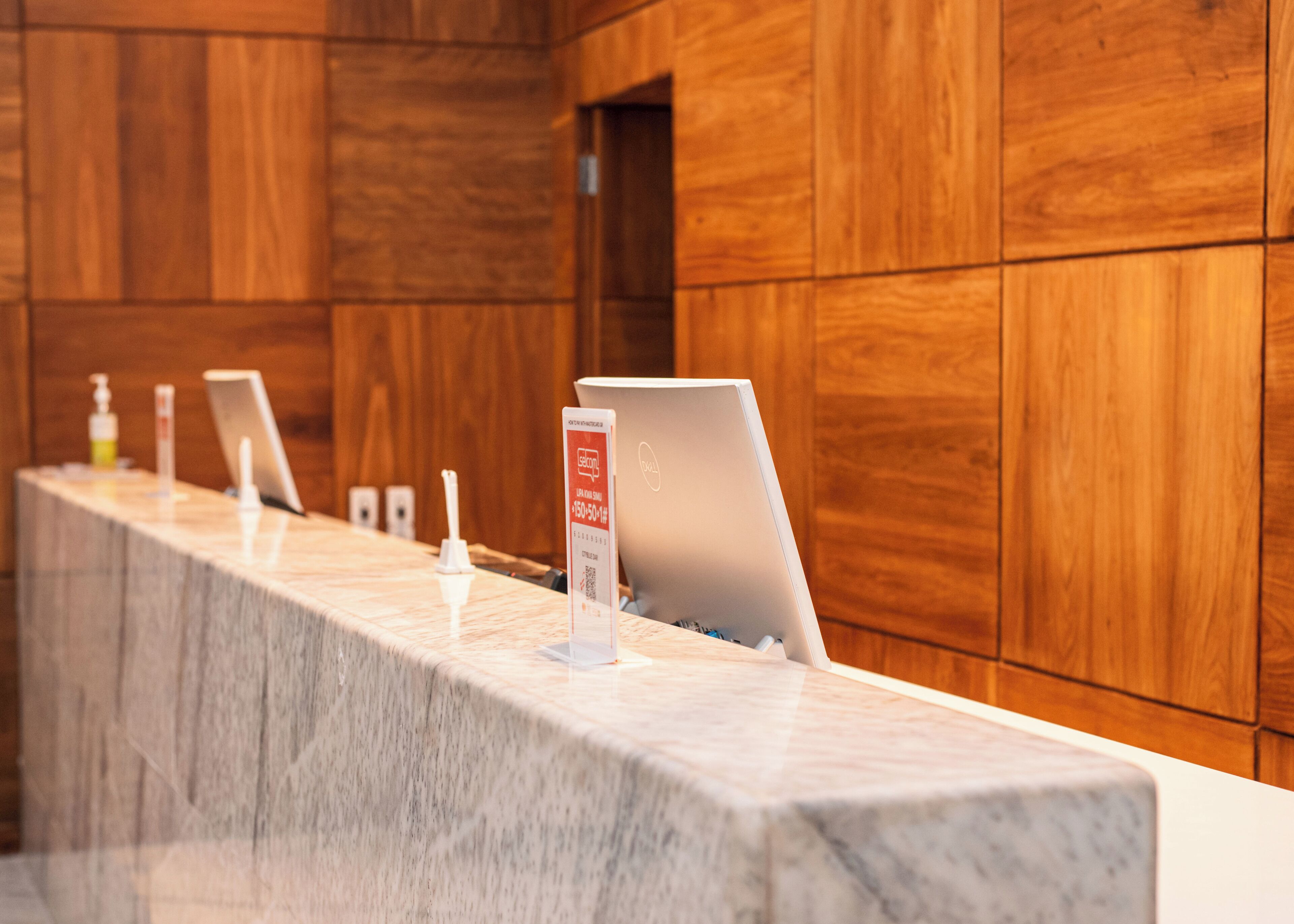 A reception desk with a laptop, a sign, and a hand sanitizer dispenser.