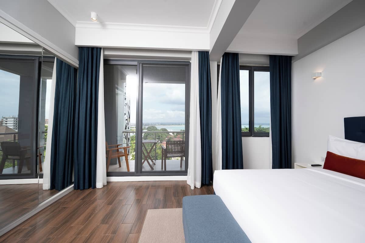 Ett modernt hotellrum med en stor säng, en balkong med utsikt och en skjutdörr i glas.