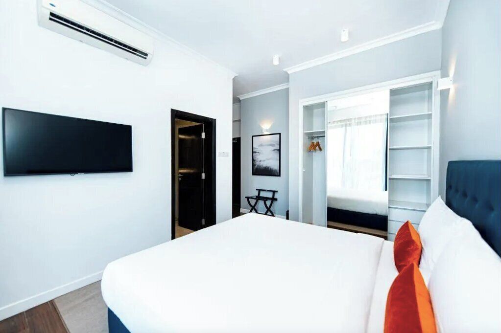A modern bedroom with a bed, a TV mounted on the wall, a wardrobe, and a door leading to another room.