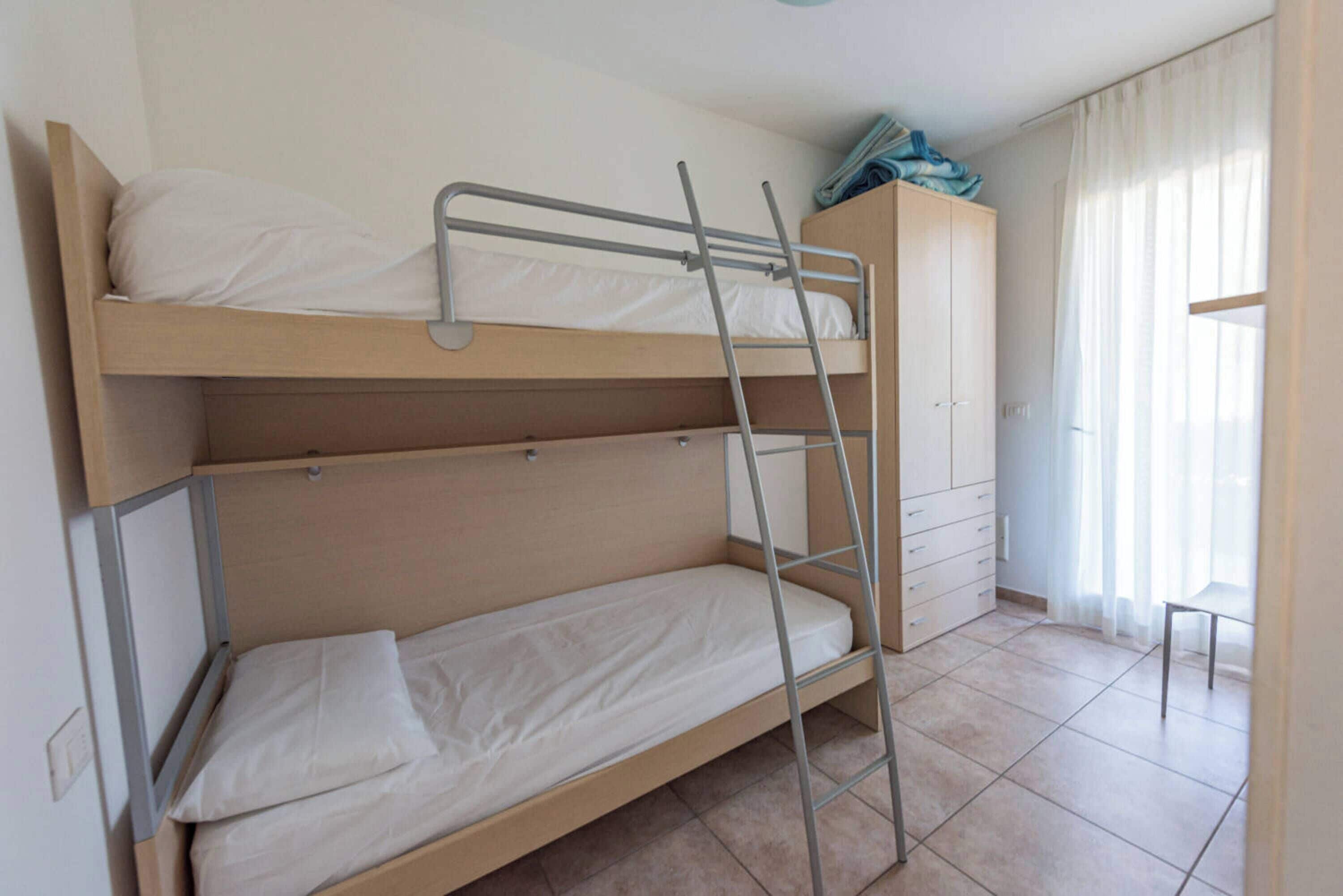 A bunk bed room with a ladder, a wooden wardrobe, and a chair.