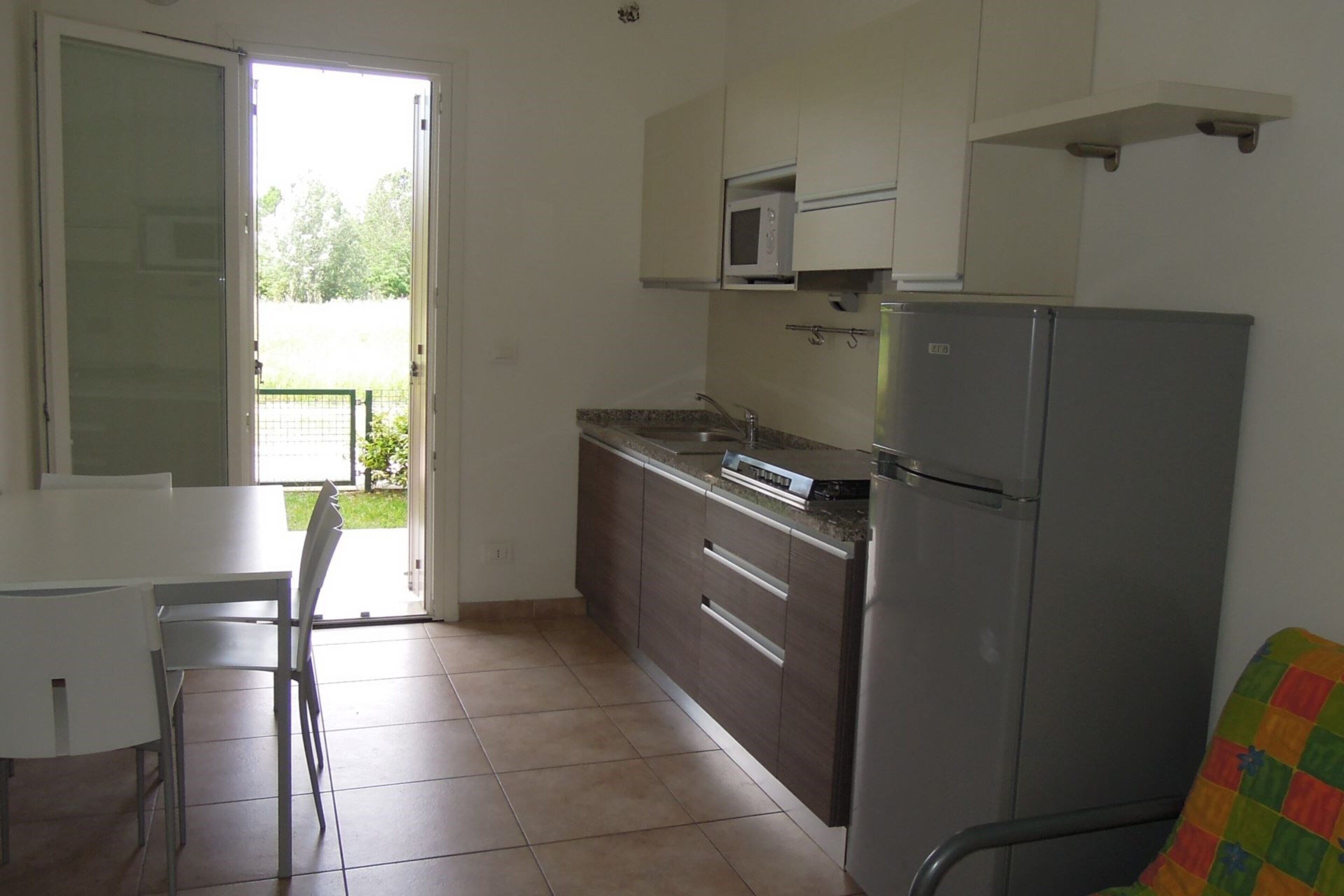 Una cocina con refrigerador, microondas y una mesa de comedor con sillas.