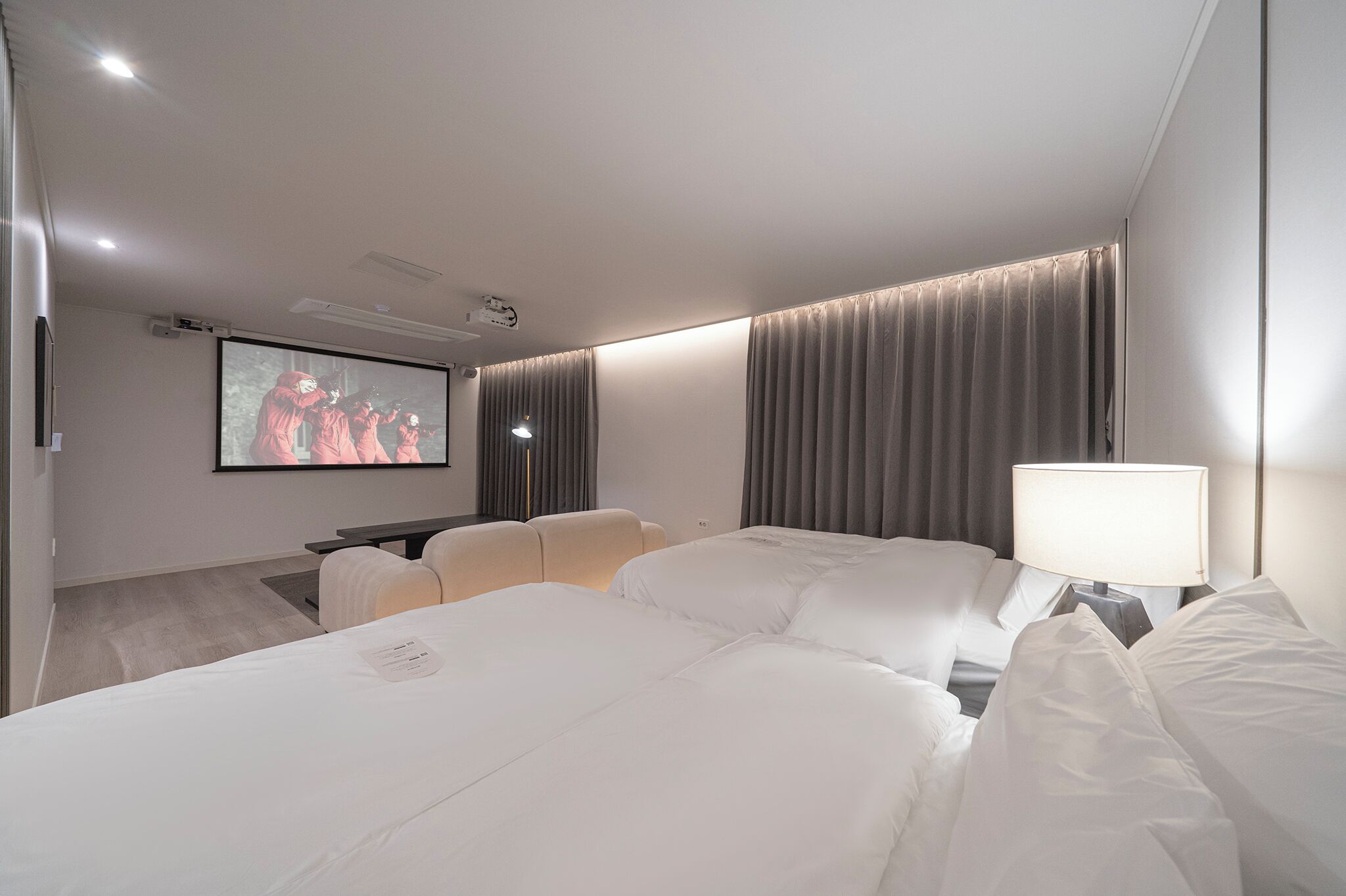 A hotel room with a large bed, a desk, a chair, a TV screen, and curtains.