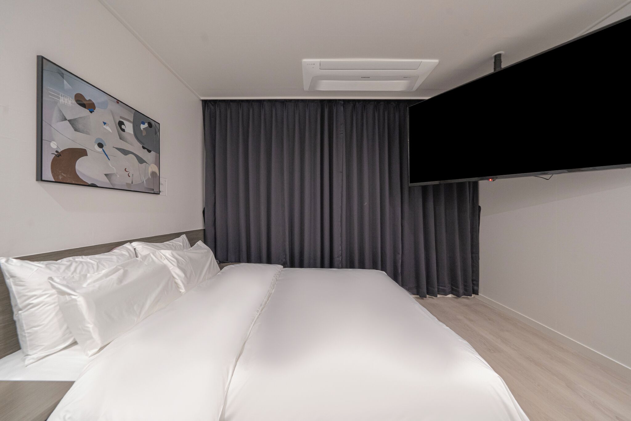 A modern hotel room with a large bed, a flat-screen TV mounted on the wall, and a painting above the bed.
