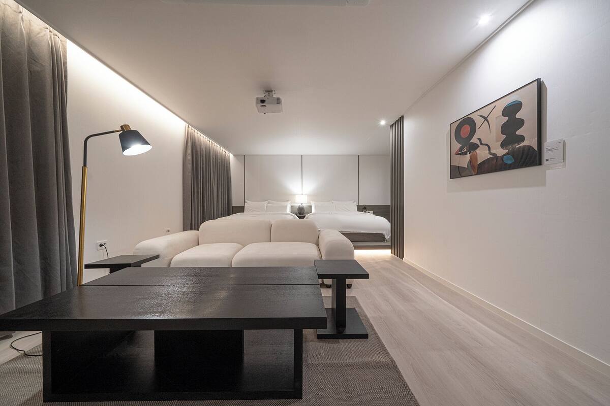 A modern hotel room with a large bed, a desk, a lamp, and a painting on the wall.