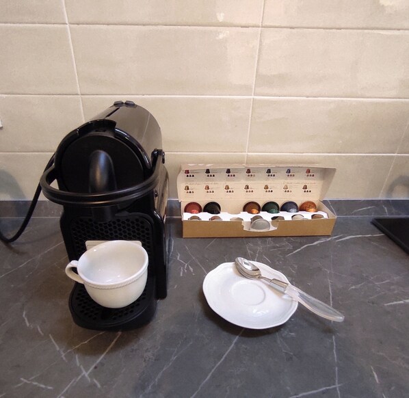 Une machine à café, une tasse, une assiette avec une cuillère et une boîte de dosettes de café sur un plan de travail de cuisine.