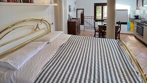 Une chambre à coucher avec un lit, une lampe de chevet, une bibliothèque remplie de livres et une vue sur la cuisine par le biais d’une arche.