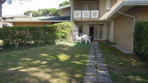 Ein Wohngebäude mit einem gepflasterten Weg, der zu einer kleinen Terrasse mit Gartenmöbeln führt.