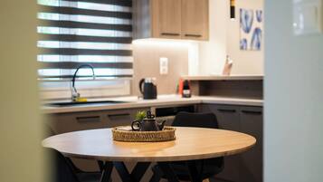 A modern kitchen with a round wooden table, a woven placemat, a teapot, and a small plant.