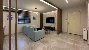 Una sala de estar moderna con un sofá, un televisor instalado en una pared de ladrillo y una puerta.