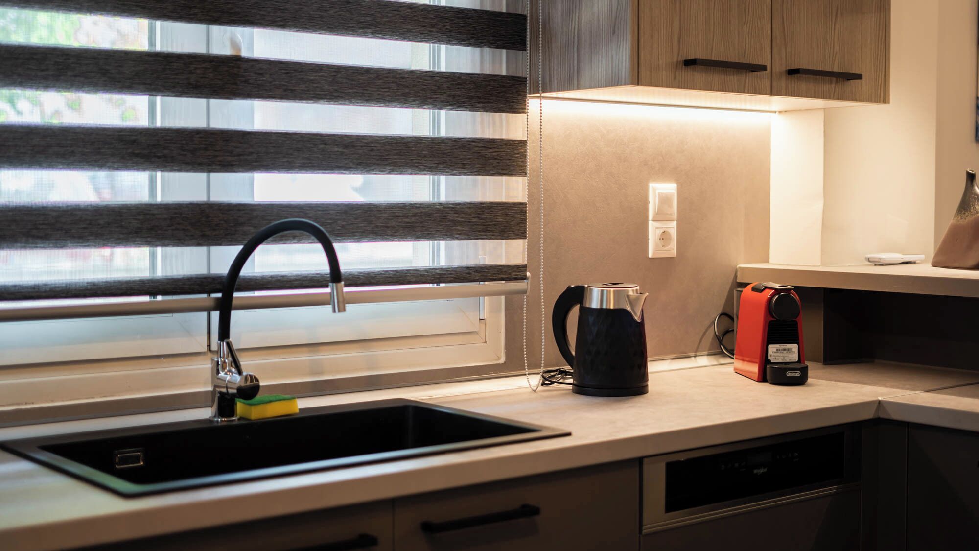 A modern kitchen with a black sink, a kettle, and a coffee maker on the counter.